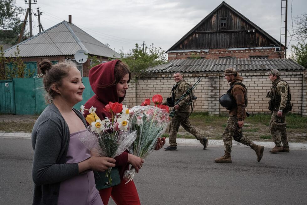 Ukrainian soldiers pass by as Polina (R), 15, and her cousin Nastya, 16, bring flowers to Polina's mother to celebrate her birthday as heavy shelling can be heard in the distance in Raihorodok.