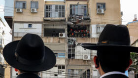 Ultra-Orthodox Jewish men watch as Israeli security forces and first responders inspect a building hit by an Iranian projectile strike at a residential neighbourhood in Bnei-Brak, on the eastern outsk