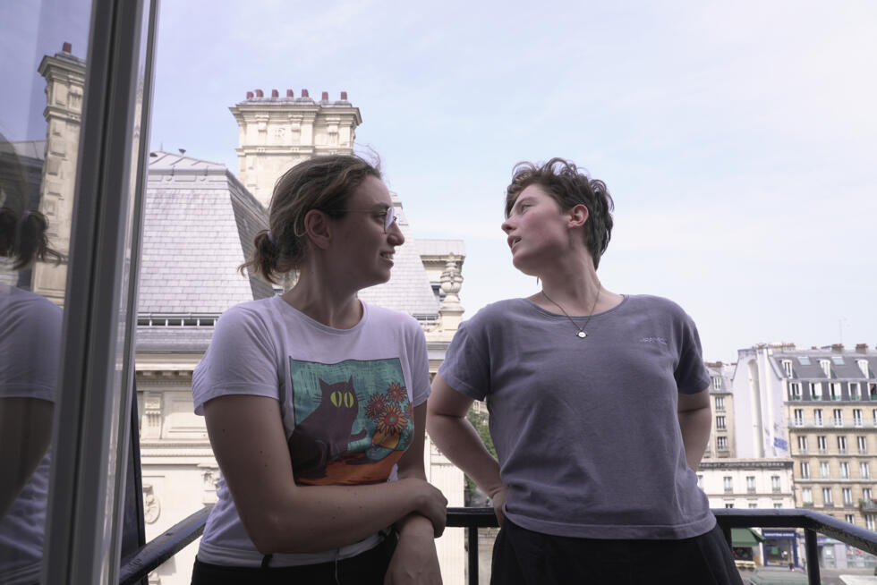 Amelie Kenney, right, and her partner Francesca Pilia stand on the balcony of the attic apartment they share in Paris.
